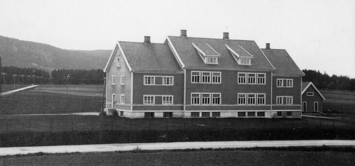 Svart-hvitt foto av Korsmo gamle skole. åpent landskap med jorder og skog i området rundt