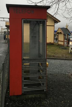 Rød telefonkiosk foran stasjonen. Bildet er tatt en grå regnværsdag