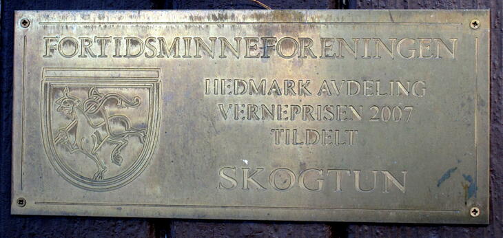 Plakett med tekst: Fortidsminneforeningen. Hedmark avdeling. Verneprisen 2007. Tildelt Skogtun