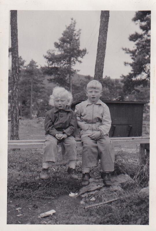 To små gutter med lyst hår sitter på en benk ved Buggebanen