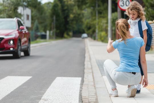 Mor og datter snakker sammen ved et fotgjengerfelt mens en bil passerer i bakgrunnen