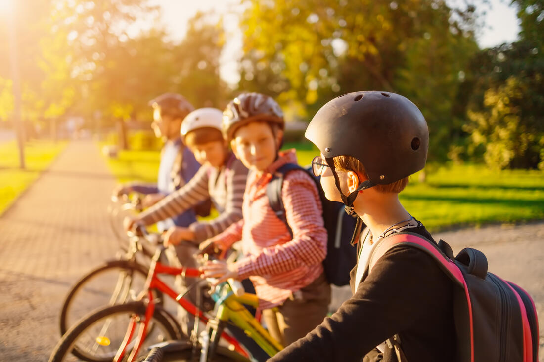 Barn på sykkel, med hjelm og sekk. 