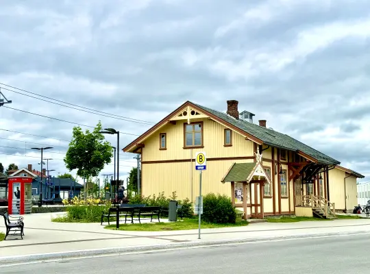 Stasjonsbygningen på Skarnes med en gammel telefonkiosk og toglinjene i bakgrunnen