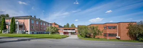 Glommatunet, vidvinkel foto av bygget sett mot inngangspartiet. Blå himmel og grønt gress. 