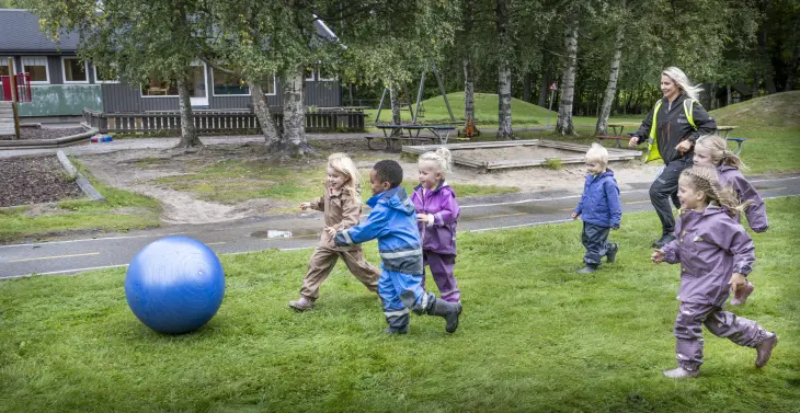 Barn i barnehagen spinger etter stor, blå ball på gressplenen