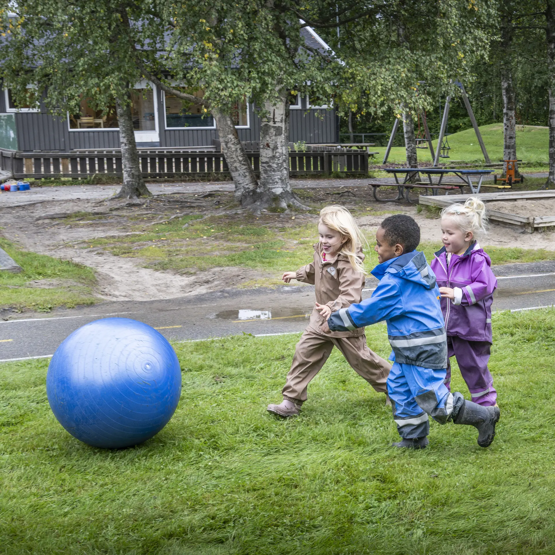 Tre barn i barnehagen løper etter en stor, blå ball